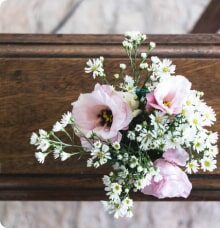 En bukett med rosa blommor och små vita blommor ligger på en träyta.