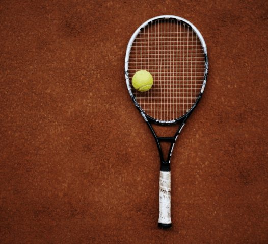 Tennisracket och en gul tennisboll på en grusplan.